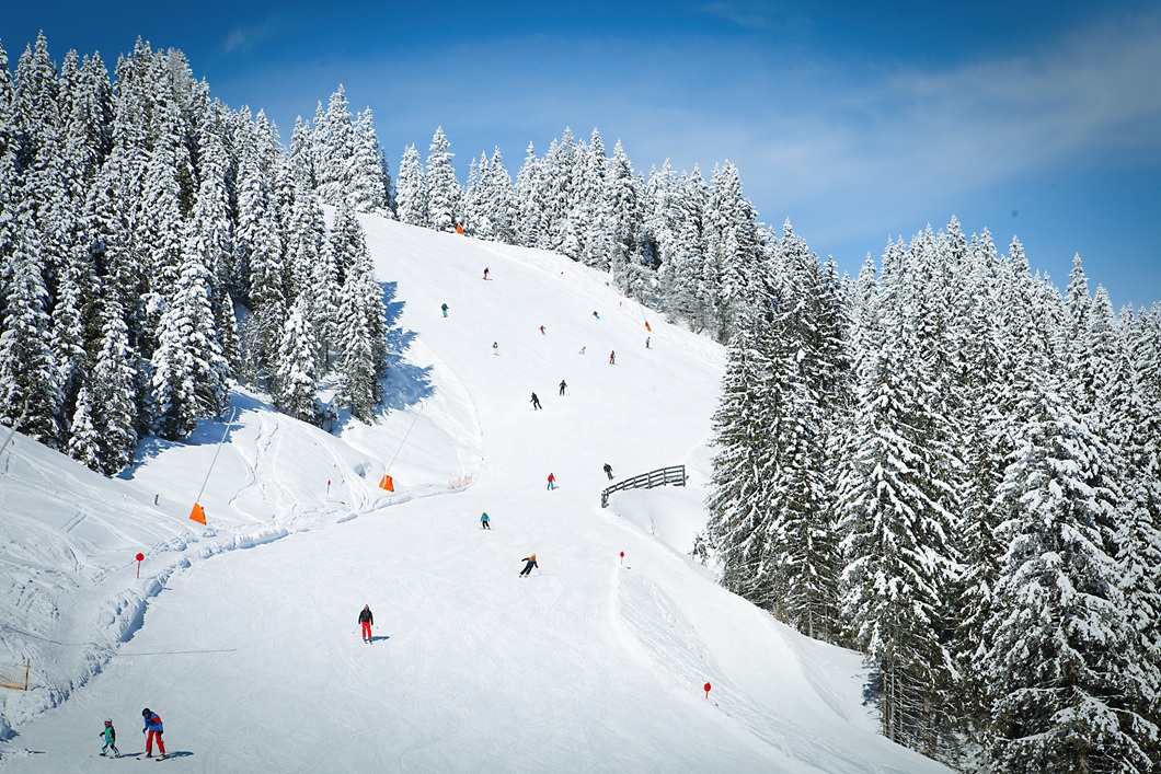 Blick auf eine Skipiste mit Skifahrern und einer verschneiten Winterlandschaft in den Kitzbühler Alpen