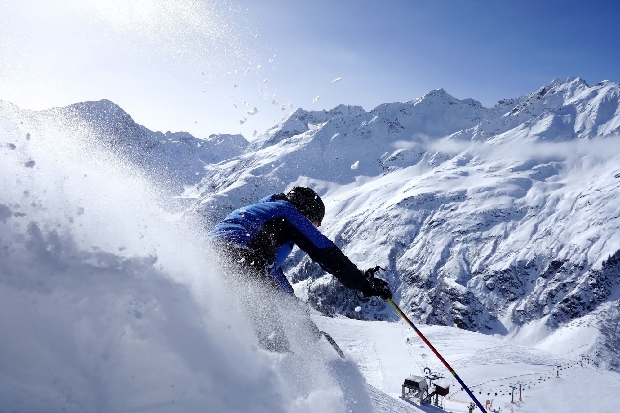 Ein Skifahrer fährt rasant auf einer Piste mit scheebedeckten Bergen im Hintergrund